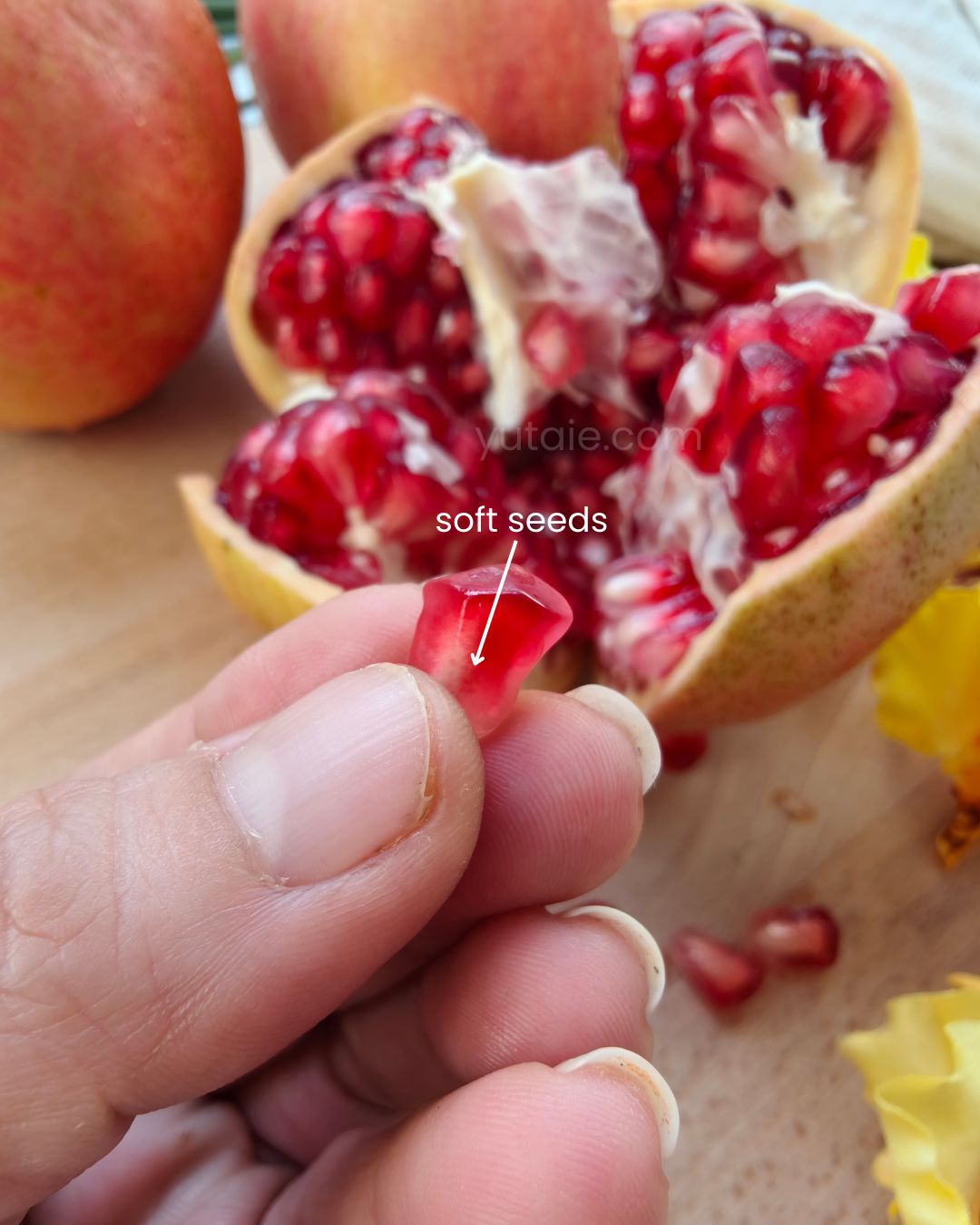 Pomegranate with soft seeds being held by a hand on a wooden surface.